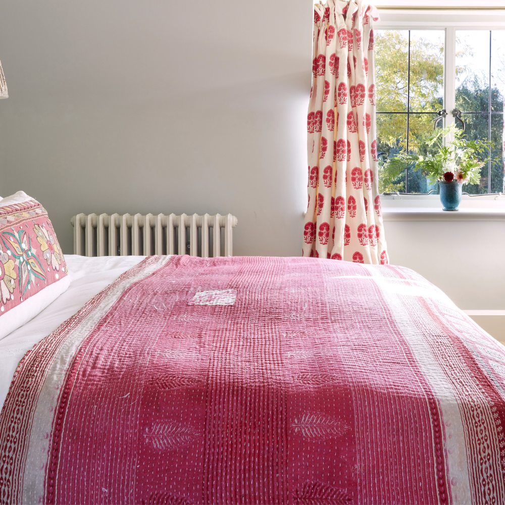 a comfy bed with white bedsheets and a pink throw, with embroidered cushions in a light and airy room
